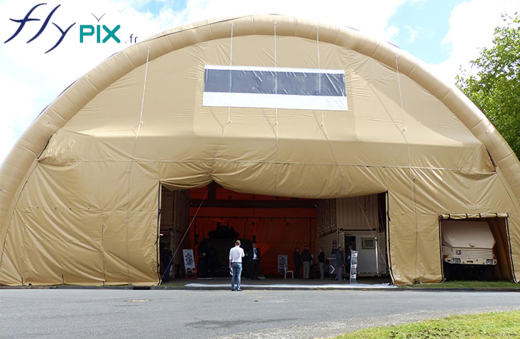 Hangar gonflable industriel, en forme de tunnel, avec une large ouverture, pour faire circuler des machines ou des véhicules.