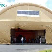 Hangar gonflable industriel, en forme de tunnel, avec une large ouverture, pour faire circuler des machines ou des véhicules.