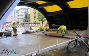 Tente de chantier gonflable: des ouvriers travaillent la pose de béton au sol, en étant protégé de la pluie et des intempéries.