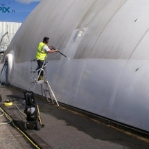 En environnement extérieur, un technicien procède à la réparation d'une ancienne toiture d'un hangar gonflable.