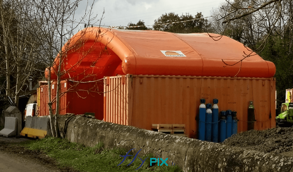 Préau gonflable en forme de demi-lune, très solide et très résistante, entre 1 containers maritimes.