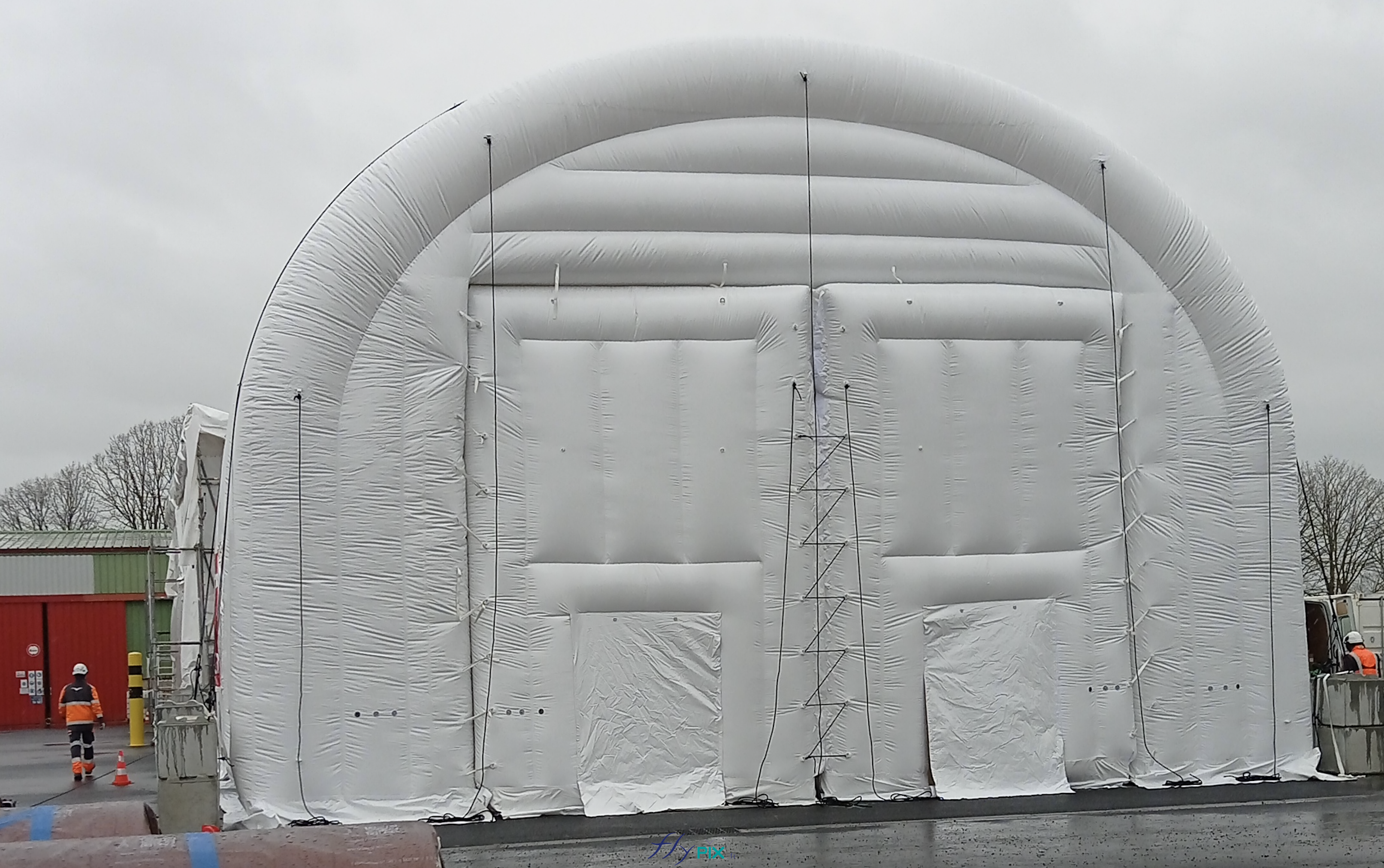 Une vue générale de la face avant du hangar gonflable, avec 2 grandes portes larges pignons, qui sont en fait 2 modules amovibles pour faire une ouverture principale plus grande. Les cordes de haubanage sont fixés à des anneaux et des oeillets de fixation métalliques ; elles sont prêtes à être fixées aux blocs de bétons (lestages au sol). - Droits réservés, copyrights FLYPIX.