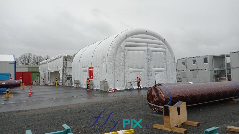 Sur cette photo, les opérateurs sont entrain de mettre en place les lestages, des blocs de béton et aussi de procéder aux raccordements de cordes de haubanage (cordes marine pro Lancelin, très robustes), via les anneaux et les oeillets de fixations répartis le long des boudins d'osssatures de la tente gonflable. - Droits réservés, copyrights FLYPIX.