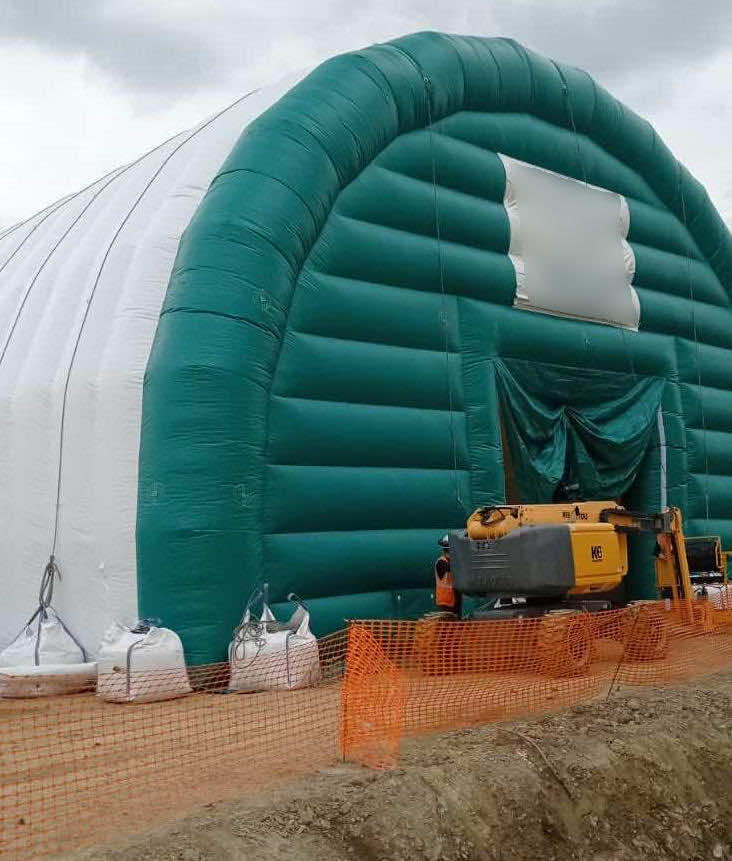 , Chantier de dépollution de site : 2 modules de hangar gonflable de S = 200 m2, soit S = 400 m2 de surface utile de travail,  Sur cette photo c-desosus, vous pouvez observer sur la pignon AV de l’abri gonflable une grande porte d’accès principale de L = 5 m x H = 5 m, en enveloppe PVC. La tente gonflable est un très grand modèle de grandes surfaces et de grandes dimensions, comme le montre l’échelle par rapport à la taille des techniciens présents pendant le déploiement et l’installation de la tente. Cette grande porte permet d’assurer l’accès des machines de chantier pour l’excavation et la dépollution des sols. Photo : copyright FlyPix/Vivien LAÏLLE, droits réservés.