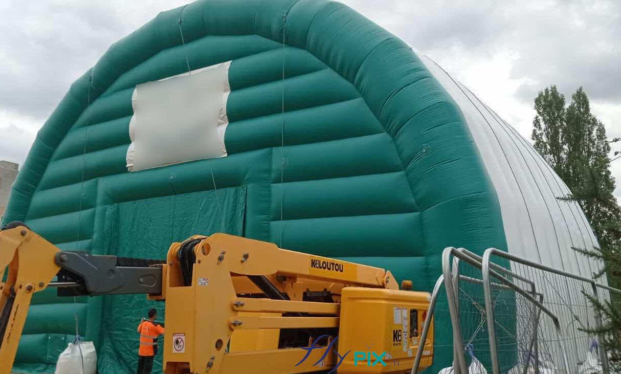 , Chantier de dépollution de site : 2 modules de hangar gonflable de S = 200 m2, soit S = 400 m2 de surface utile de travail,  Sur cette photo c-desosus, vous pouvez observer sur la pignon AV de l’abri gonflable une grande porte d’accès principale de L = 5 m x H = 5 m, en enveloppe PVC. La tente gonflable est un très grand modèle de grandes surfaces et de grandes dimensions, comme le montre l’échelle par rapport à la taille des techniciens présents pendant le déploiement et l’installation de la tente. Cette grande porte permet d’assurer l’accès des machines de chantier pour l’excavation et la dépollution des sols. Photo : copyright FlyPix/Vivien LAÏLLE, droits réservés.