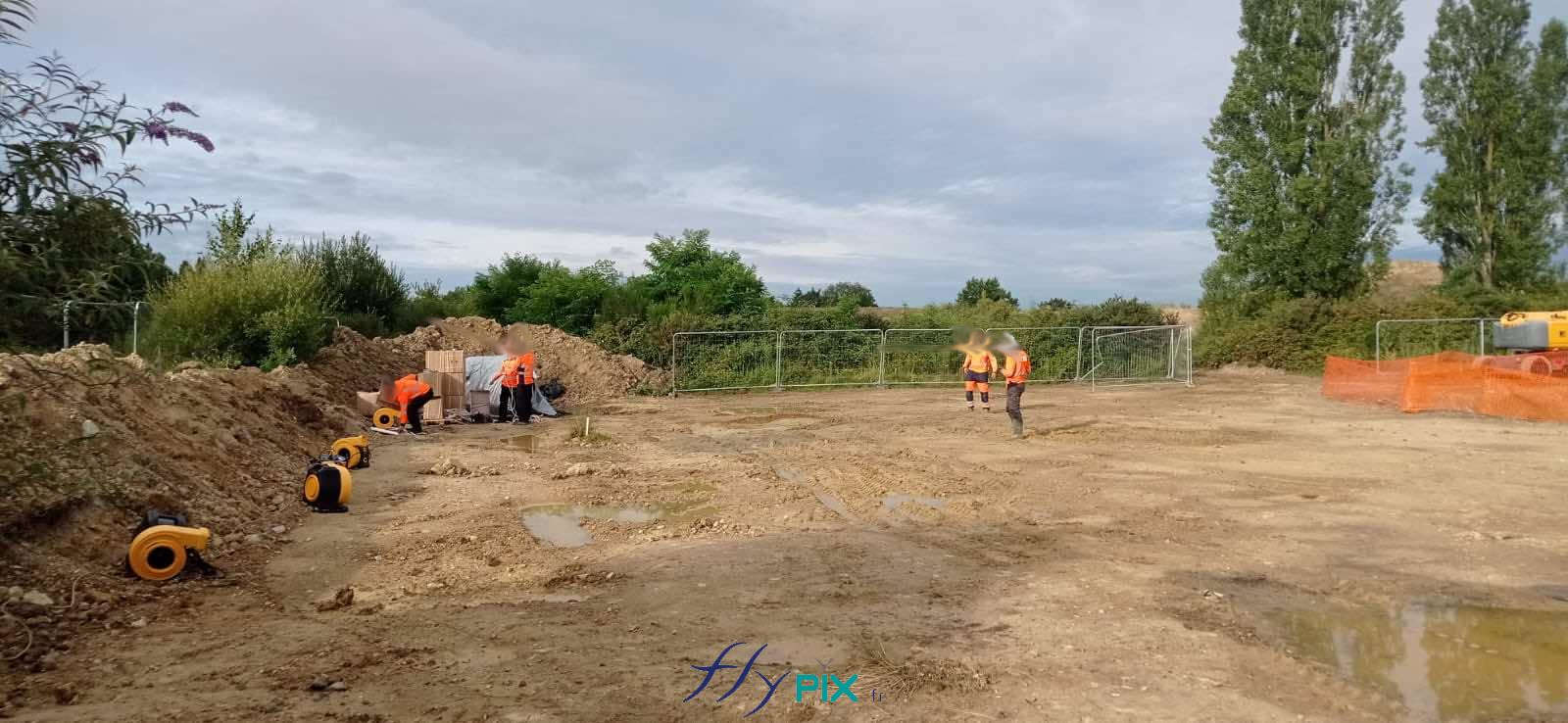 , Chantier de dépollution de site : 2 modules de hangar gonflable de S = 200 m2, soit S = 400 m2 de surface utile de travail,  Avant la mise en place des tentes gonflables de chantier, les techniciens et les opérateurs nivellent le terrain pour l’aplanir, ils contrôlent la présence d’objets contondants au sol pour les enlever si nécessaire. Ils positionnent ensuite les turbines et délimitent la zone qui réceptionnera la surface des modules d’abris gonflables. Ensuite, ils vont sortir les tentes de leur sac, les déplier et commencer la phase de gonflage avec les turbines électriques, qui alimentent des manchons spéciaux prévus à cet effet. Il faut 8 turbines par module de tente gonflable, parce que ce sont des grands gabarits et des grandes tailles. Les 16 turbines doivent être alimentées en permanence. Les structures gonflables ventilées en permanence sont plus résistantes aux montages / démontages répétés, aux trous et fissures dans l’enveloppe compéré à l’air captif. L’enveloppe PVC 0.45 mm est une très bonne solution pour la fabrication de hanagrs gonflables réutilisables, durables, solides, sur plusieurs chantiers. Nos techniciens privilégient des solutions en ventilé par tubrine en permenance, plutot que en air captif (pompe) – Photo : copyright FlyPix/Vivien LAÏLLE, droits réservés.