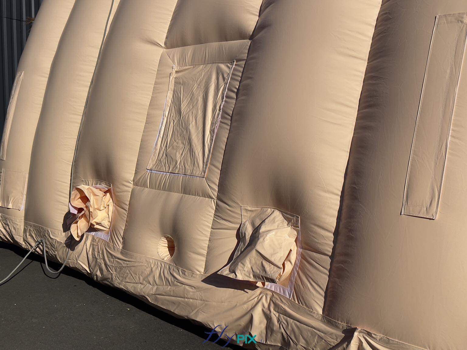 , Hangar gonflable militaire L = 25 m x l = 14 m x H = 7 m, S = 350 m2,  Une vue de la base d'un module gonflable, une photo prise depuis l'extérieur de la structure gonflable, qui montre différentes interfaces : une fenêtre avec un volet amovible et pliable, 2 manchons à air, et 1 trou passe fils et gaines électriques. - Copyright : Vivien LAÏLLE/FLYPIX, droits réservés.