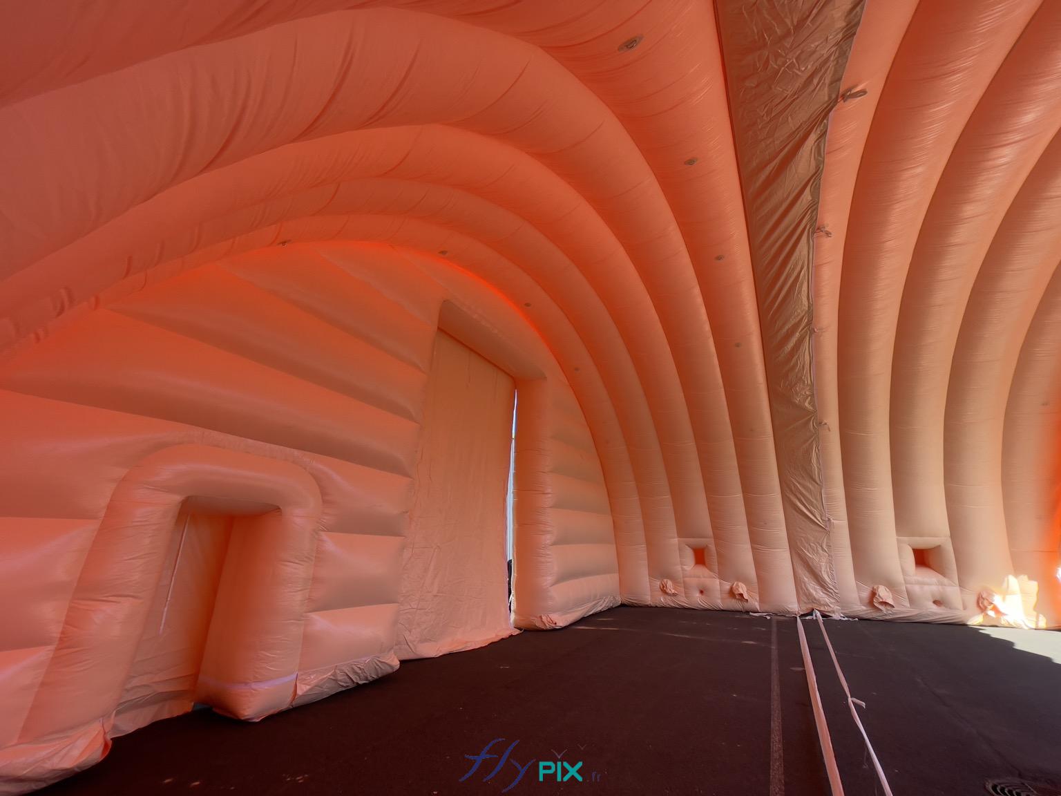 , Hangar gonflable militaire L = 25 m x l = 14 m x H = 7 m, S = 350 m2,  Une prise de vue photo générale qui montre 2 modules de hangar gonflable militaire assemblés et connectés, avec le raccordement par l'intérieur qui assure l'étanchéité de la toiture en cas de pluies ou d'intempéries. À gauche, nous voyons la petite porte secondaire de service, ensuite la grande porte d'accès principale, sur le pignon avant. Au fond, sur chaque module, dans la partie inférieure, nous pouvons observer les fenêtres et les manchons à air et les trous passe fils et gaines électriques. - Copyright : Vivien LAÏLLE/FLYPIX, droits réservés.