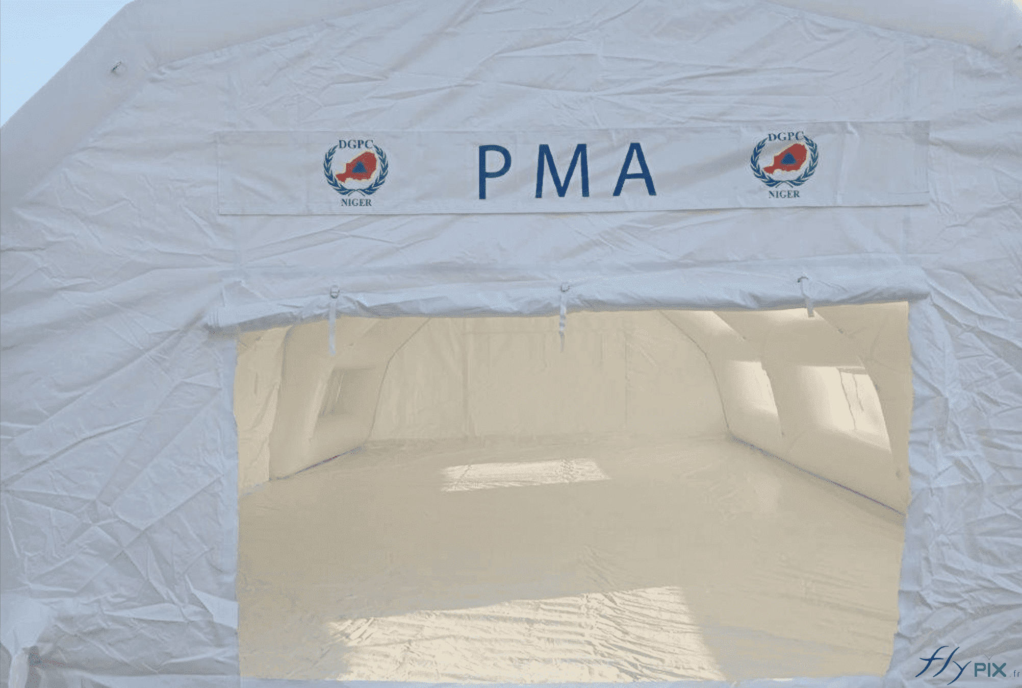 Au-dessus de la porte, il y a une banderole de marquage amovible imprimée avec le logo. C'est une bâche imprimée qui est fixée par des bandes Velcro sur l'enveloppe de la tente gonflable. La porte peut être remontée et pliée. Dans le prolongement, à l'intérieur, la bâche amovible au sol est visible. Au-dessus de la porte, il y a une banderole de marquage amovible imprimée avec le logo. C'est une bâche imprimée qui est fixée par des bandes Velcro sur l'enveloppe de la tente gonflable. La porte peut être remontée et pliée. Dans le prolongement, à l'intérieur, la bâche amovible au sol est visible.