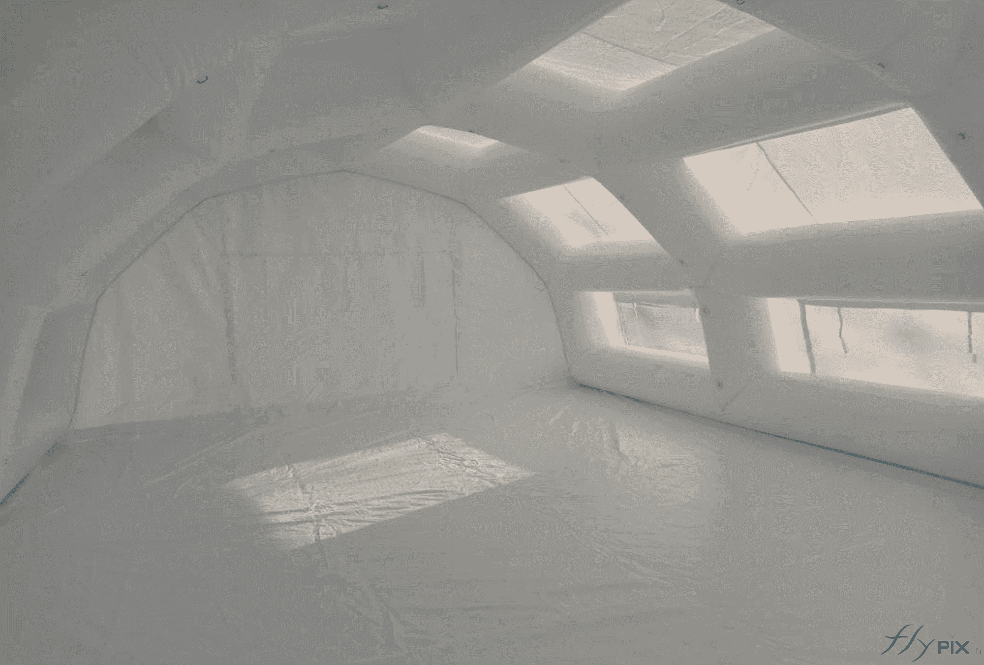 Une vue de l'intérieur de la tente gonflable PMA de surface S = 60 m2, avec une bâche au sol en PVC, amovible. Les boudins d'ossature, squelette de l'abri gonflable procurent une très grande solidité et robustesse à la structure gonflable. Ils sont tous interconnectés et ils présentent, à des espacements réguliers, des anneaux et des œillets métalliques de fixation, très utiles pour y attacher des accessoires médicaux, ou des dispositifs éclairages LED. Notez que l'enveloppe en PVC de couleur blanche et la présence de points de jour et de fenêtres permettent d'obtenir une lumière intérieure naturelle et diffuse. Une vue de l'intérieur de la tente gonflable PMA de surface S = 60 m2, avec une bâche au sol en PVC, amovible. Les boudins d'ossature, squelette de l'abri gonflable procurent une très grande solidité et robustesse à la structure gonflable. Ils sont tous interconnectés et ils présentent, à des espacements réguliers, des anneaux et des œillets métalliques de fixation, très utiles pour y attacher des accessoires médicaux, ou des dispositifs éclairages LED. Notez que l'enveloppe en PVC de couleur blanche et la présence de points de jour et de fenêtres permettent d'obtenir une lumière intérieure naturelle et diffuse.