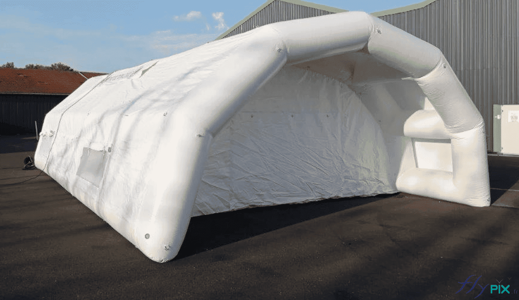 Sur cette photo qui présente une vue de la façade du pignon avant de l'abri gonflable PMA, il est possible d'observer une grande porte d'accès principale protégée par une marquise. Cette extension est utile pour le déchargement des brancards à l'arrière des véhicules de secours (pompiers, hôpitaux et ambulanciers), pour protéger les patients, malades ou accidentés de la pluie et des intempéries pendant l'entrée dans la tente gonflable. Sur cette photo qui présente une vue de la façade du pignon avant de l'abri gonflable PMA, il est possible d'observer une grande porte d'accès principale protégée par une marquise. Cette extension est utile pour le déchargement des brancards à l'arrière des véhicules de secours (pompiers, hôpitaux et ambulanciers), pour protéger les patients, malades ou accidentés de la pluie et des intempéries pendant l'entrée dans la tente gonflable.