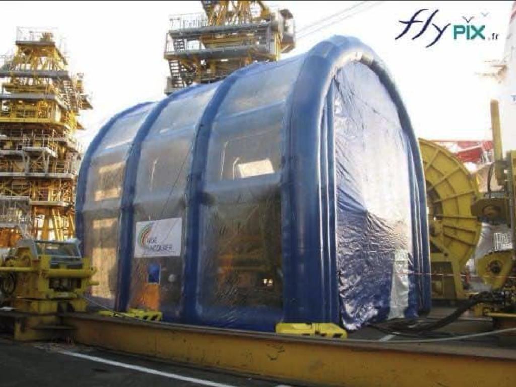 Grand hangar gonflable en forme de U-inversé, avec une grande hauteur et une grande largeur, fabriqué pour la société TECHNIP. Un abri gonflable pour un chantier naval dans un port, pour la maintenance et le nettoyage d'un gros moteur de bâteau en milieu confiné et protégé des intempéries.