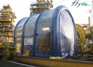 Grand hangar gonflable en forme de U-inversé, avec une grande hauteur et une grande largeur, fabriqué pour la société TECHNIP. Un abri gonflable pour un chantier naval dans un port, pour la maintenance et le nettoyage d'un gros moteur de bâteau en milieu confiné et protégé des intempéries.