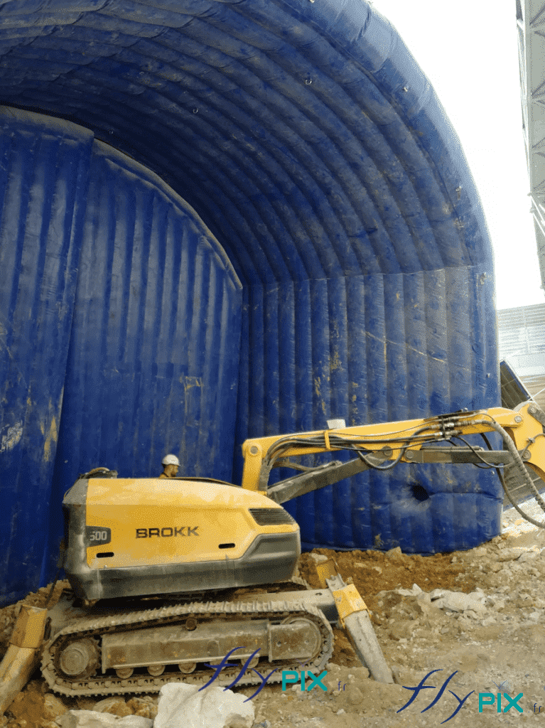 Un exemple de réalisation d'un mur gonflable de réduction de bruits et des nuisances sonores, en forme de demi-dôme, avec au premier plan une pelleteuse déployée lors d'un chantier à Monaco. Un exemple de réalisation d'un mur gonflable de réduction de bruits et des nuisances sonores, en forme de demi-dôme, avec au premier plan une pelleteuse déployée lors d'un chantier à Monaco.