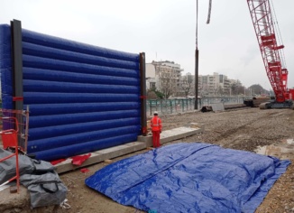 Grand Paris Express, chantier urbain de Meudon : cette photo est intéressante parce qu'elle montre plusieurs choses essentielles qui concerne les structures gonflable de murs de réduction de bruits. Premièrement, au premier plan, au sol, un écran gon flable est déployé sur toute sa surface, dans l'attente de son gonflage à l'air avec une pompe électrique. C'est une structure air captif. Deuxièmement, en arrière plan, nous observons un mur gonflé, positionné verticalement sur une structure en béton et avec des poutres métalliques. Cette configuration procure une très grande résistance structurelle aux vents, tout en minimisant au maximum l'emprise au sol, en limitant la présence et l'utilisation de sacs de lestages à remplir de sable. Tout en conservant une grande mobilité et un très bon réemploi.
